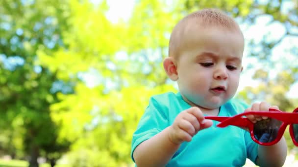 Niedlicher kleiner Junge spielt mit roter Sonnenbrille — Stockvideo