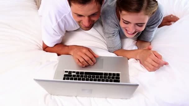 Gelukkige paar liggend op bed met behulp van laptop samen — Stockvideo