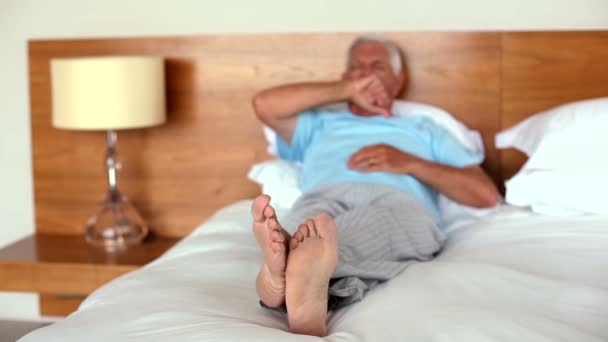 Senior homem deitado na cama bocejando e alongamento — Vídeo de Stock