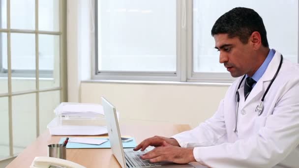 Doctor sentado en el escritorio escribiendo en el portátil — Vídeos de Stock