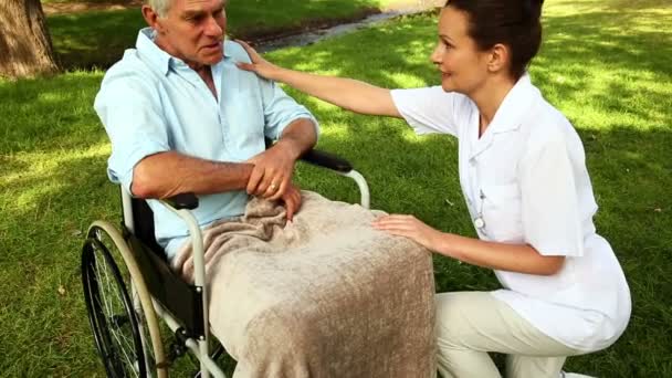 Sairaanhoitaja puhuu miehelle pyörätuolissa ulkona — kuvapankkivideo