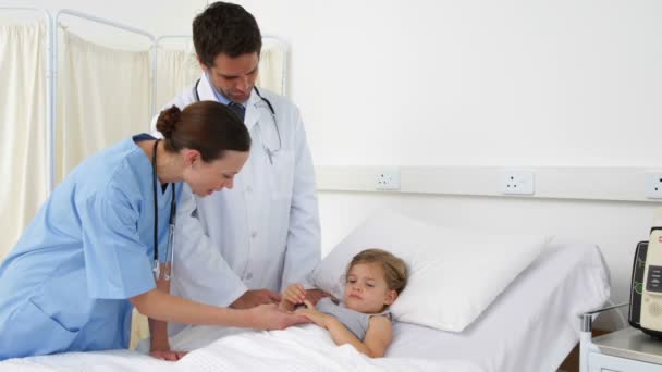 Sick little girl lying in bed talking to nurse and doctor — Stock Video