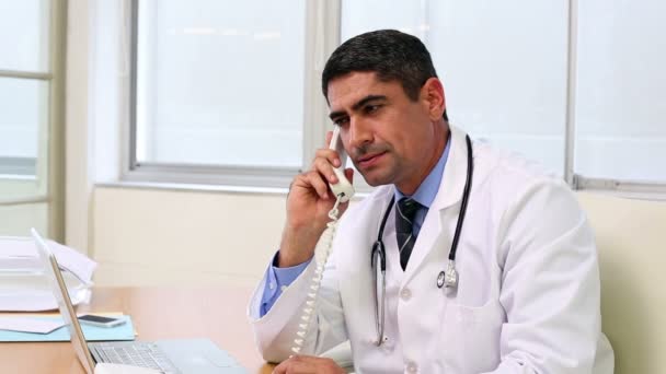 Doctor sitting at desk talking on the phone — Stock Video