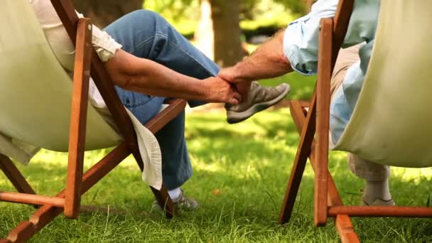 Retired couple sitting in deck chairs holding hands — Stock Video