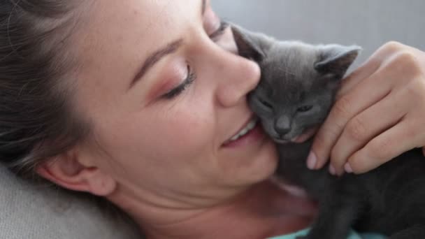 Женщина лежит на диване обнимая крошечного котенка — стоковое видео