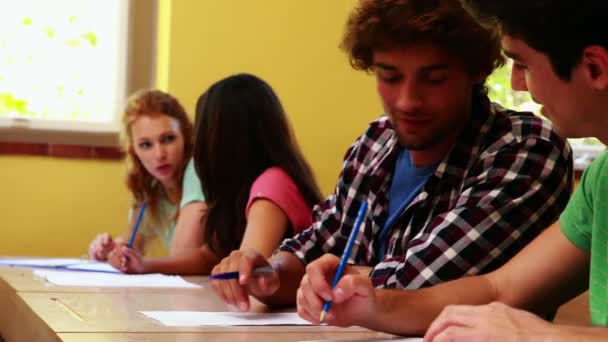 Schüler sitzen in einer Schlange, schreiben und plaudern im Klassenzimmer — Stockvideo