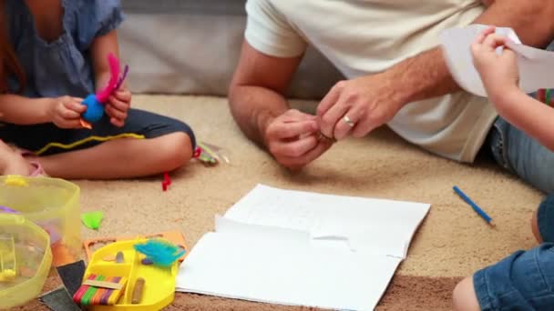 Siblings doing arts and crafts on the rug with parents — Stock Video