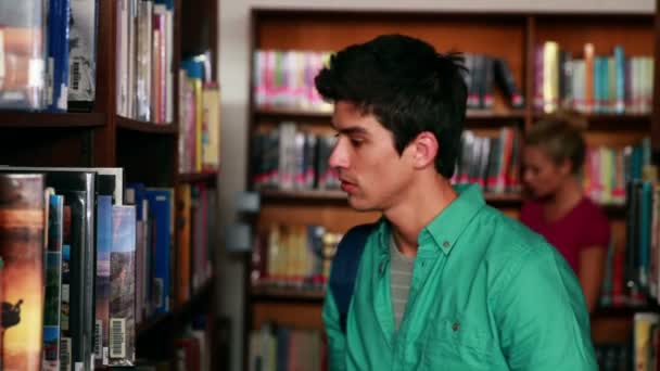 Handsome student picking out a book in the library — Stock Video