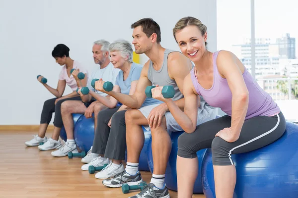 Klasse met halters zittend op oefening ballen in de sportschool — Stockfoto