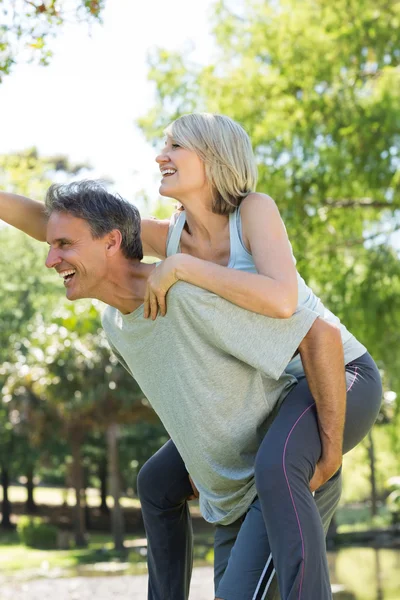 Paar genieten van piggyback rijden in park — Stockfoto