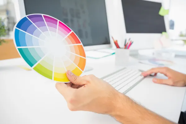 Hand holding color wheel while using computer — Stock Photo, Image