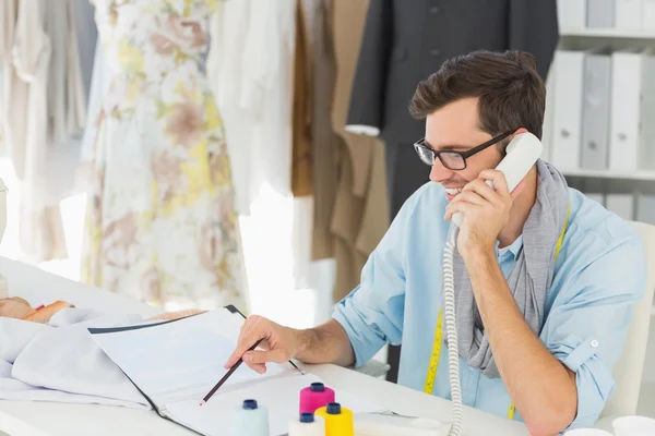 Χαμογελώντας αρσενικό σχεδιαστής μόδας χρησιμοποιώντας το τηλέφωνο στο στούντιο — Φωτογραφία Αρχείου