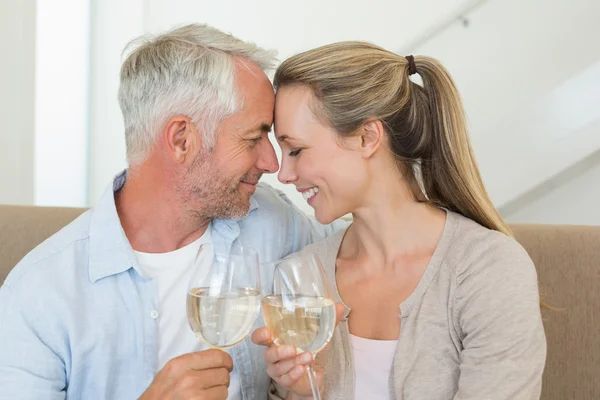 Casal feliz sentado no sofá brindar com vinho branco — Fotografia de Stock