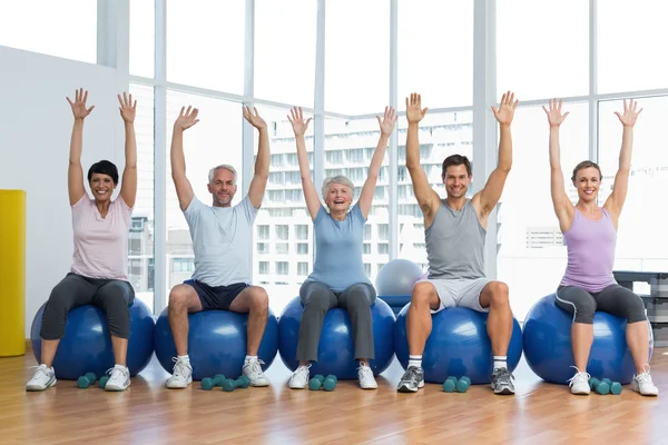 Clase sentada en bolas de ejercicio y levantando las manos en el gimnasio —  Fotos de Stock