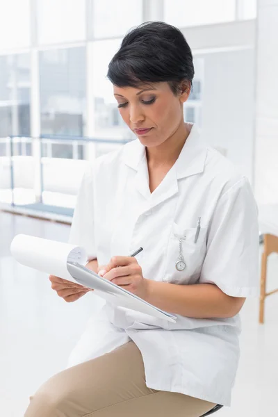 Concentrated female doctor writing on clipboard — Stock Photo, Image