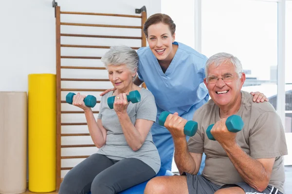 Therapist assisting senior couple with dumbbells — Stock Photo, Image