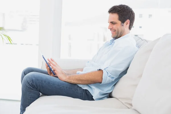 Bonito homem sentado no sofá usando seu tablet — Fotografia de Stock