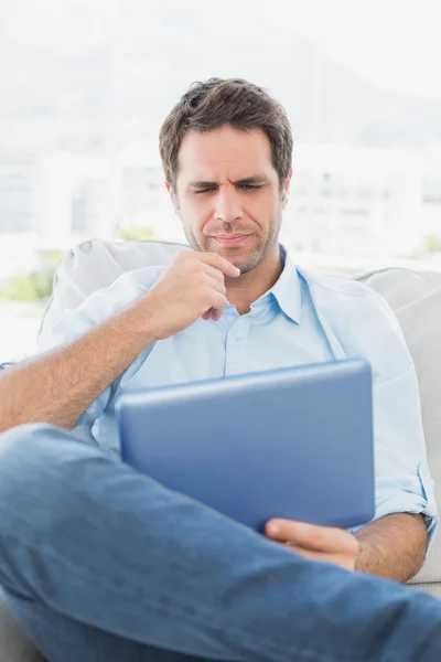 Tänkande mannen sitter i soffan med sin tablet — Stockfoto