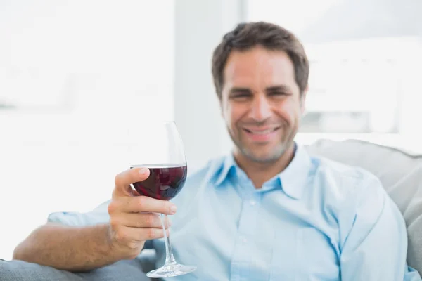 Χαρούμενος άνθρωπος χαλαρωτικό στον καναπέ με ποτήρι κόκκινο κρασί — Φωτογραφία Αρχείου