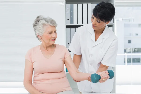 Physiotherapist assisting senior woman to lift dumbbell — Stock Photo, Image