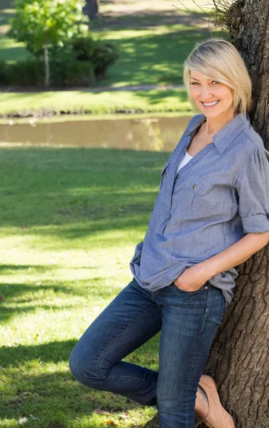 Frau lehnt sich in Park an Baumstamm — Stockfoto