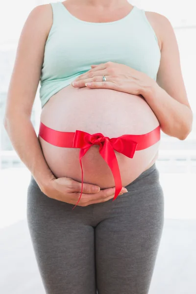 Gravid kvinna med röd rosett runt magen — Stockfoto