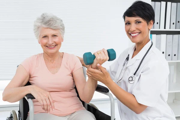 Physiotherapist assisting senior woman to lift dumbbell — Stock Photo, Image