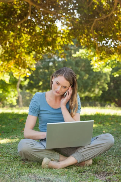 Mujer relajada usando portátil y teléfono móvil en el parque — Foto de Stock