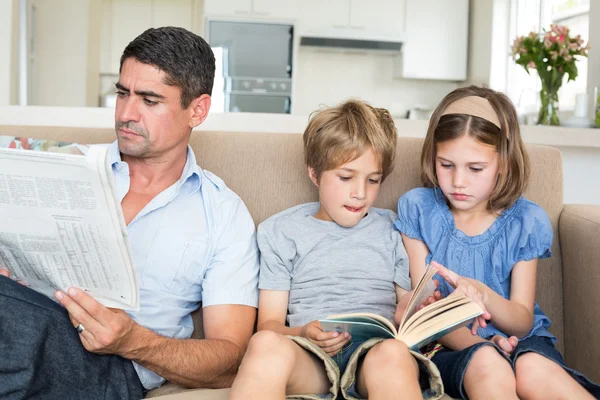Батько з газетою, діти читають книгу — стокове фото