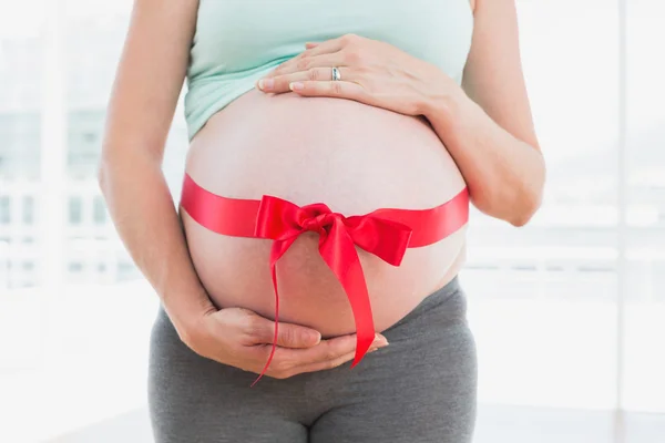 Беременная женщина с красным бантом вокруг шишки — стоковое фото