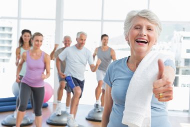 Senior woman gesturing thumbs up with people exercising clipart