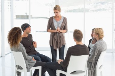Rehab group listening to woman standing up introducing herself clipart