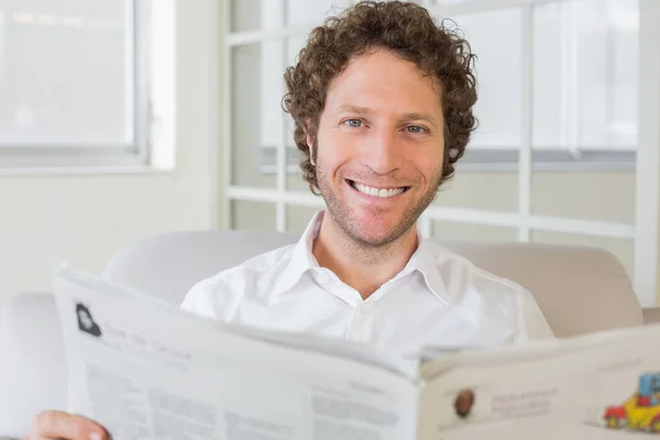 Uomo sorridente che legge il giornale a casa — Foto Stock