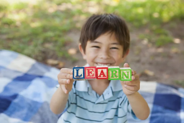 Happy boy holding block alphabets as 'learn' at park — Stock Photo, Image