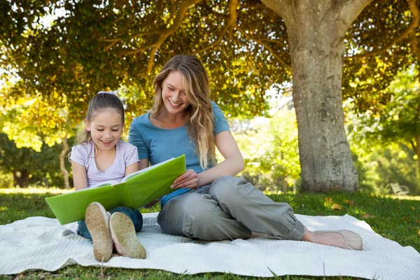 Glückliche Mutter und Tochter lesen im Park ein Buch — Stockfoto