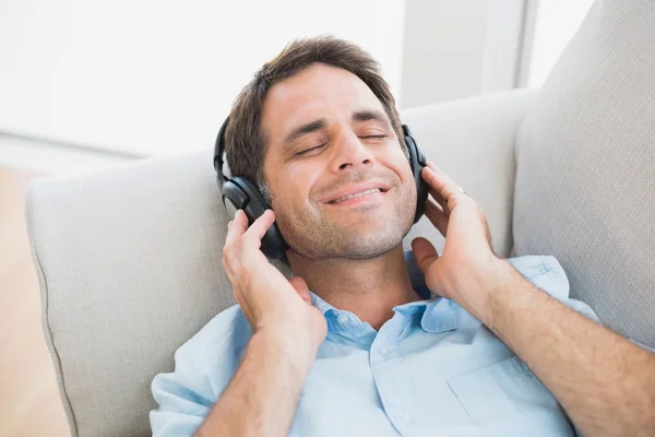 Ler stilig man liggande på soffan, lyssnar på musik — Stockfoto