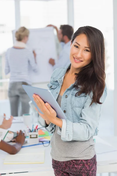 Asian woman using her tablet while her colleagues are working — Stock Photo, Image