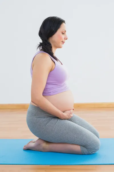 Feliz embarazada morena de rodillas en la esterilla de ejercicio — Foto de Stock