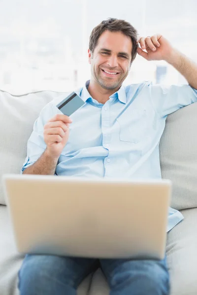 Fröhlicher Mann sitzt mit Laptop auf Sofa und kauft online ein — Stockfoto