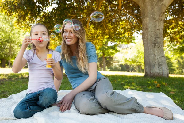 Mother with her daughter blowing soap bubbles at park — Stock Photo, Image