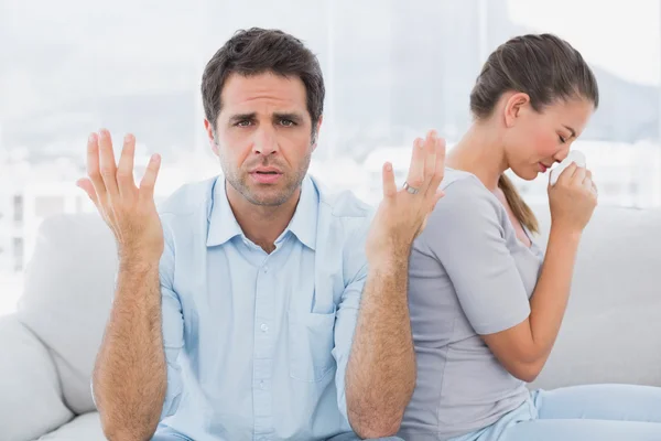 Man gesturing at camera with his crying partner on the couch — Stock Photo, Image