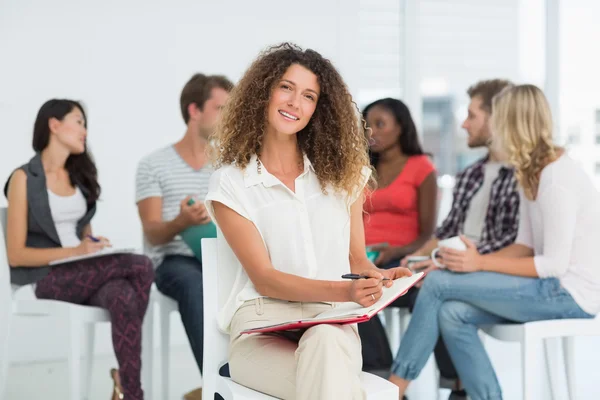 Smiling woman while colleagues are talking behind — Stock Photo, Image