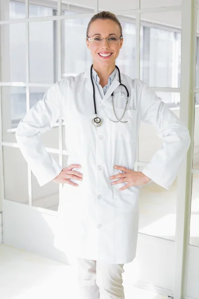 Sonriente hermosa doctora con las manos en las caderas en el hospital —  Fotos de Stock