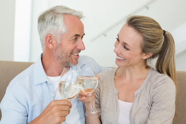 Casal feliz sentado no sofá brindar com vinho branco — Fotografia de Stock