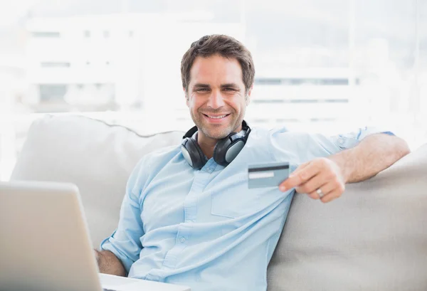 Homem bonito feliz sentado no sofá compras on-line com laptop — Fotografia de Stock