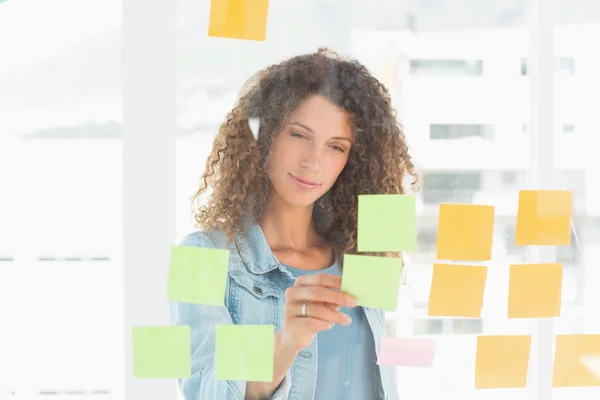 Smiling pretty designer looking at sticky notes on window — Stock Photo, Image