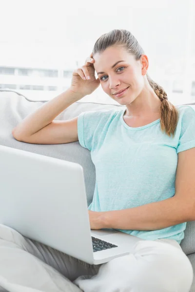 Smiling woman sitting on couch using her laptop — Stock Photo, Image