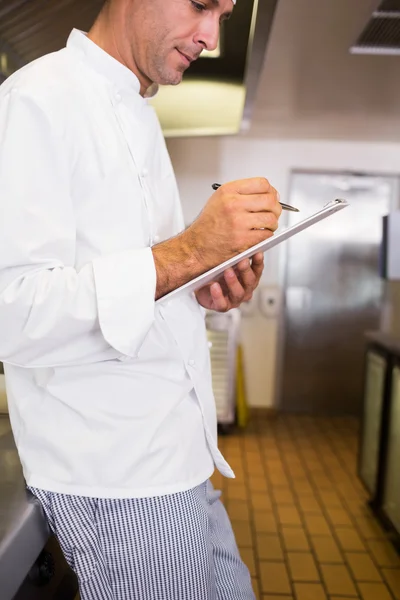 Cocinero escribiendo en el portapapeles en la cocina — Foto de Stock