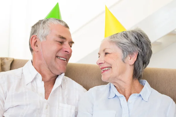 Äldre par sitter på soffan klädd partyhattar — Stockfoto