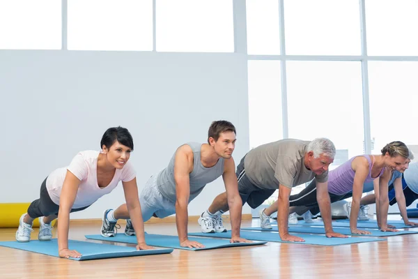 Group doing push ups in row at yoga class — Stock Photo, Image